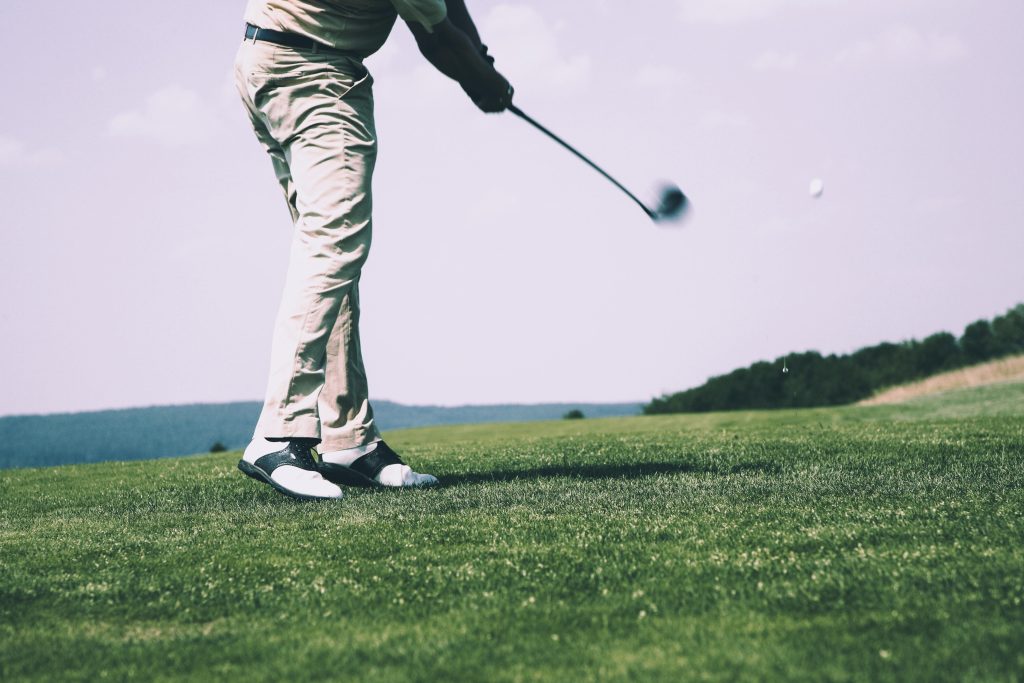 A golfer in mid-swing on a sunny day at the golf course, showing motion and focus.