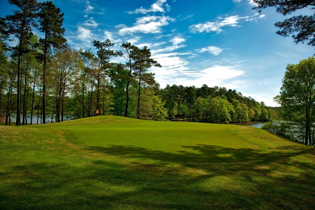 Beautiful golf course surrounded by trees and lake under a clear blue sky.